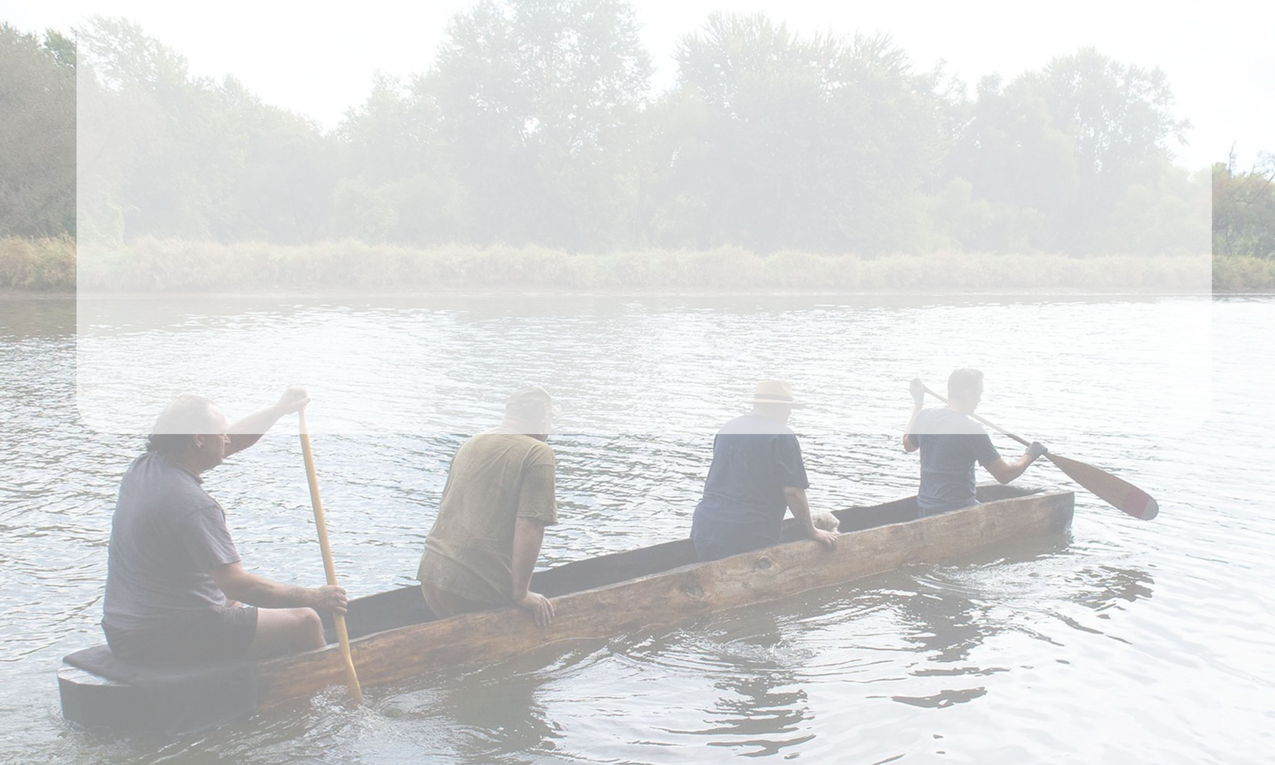 People paddling a dugout canoe on calm water.